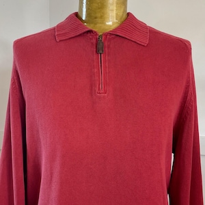 Op de afbeelding: Een rode trui met lange mouwen, een kraag en een kwart ritssluiting. De trui is gemaakt van een gebreide stof en heeft geribbelde details op de kraag en manchetten. De rits is donkerbruin.