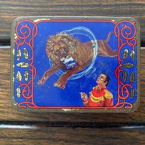 May include: A vintage tin box with a blue background and ornate gold trim. The box features a lion jumping through a hoop and a man holding a cigarette. The text on the box reads "Benson & Hedges."