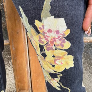 May include: Black denim pants with a floral print featuring yellow, white, and purple orchids.