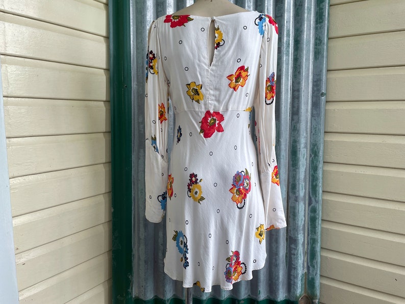 May include: A white mini dress with a floral print and a keyhole back. The dress has long sleeves and a fitted bodice.