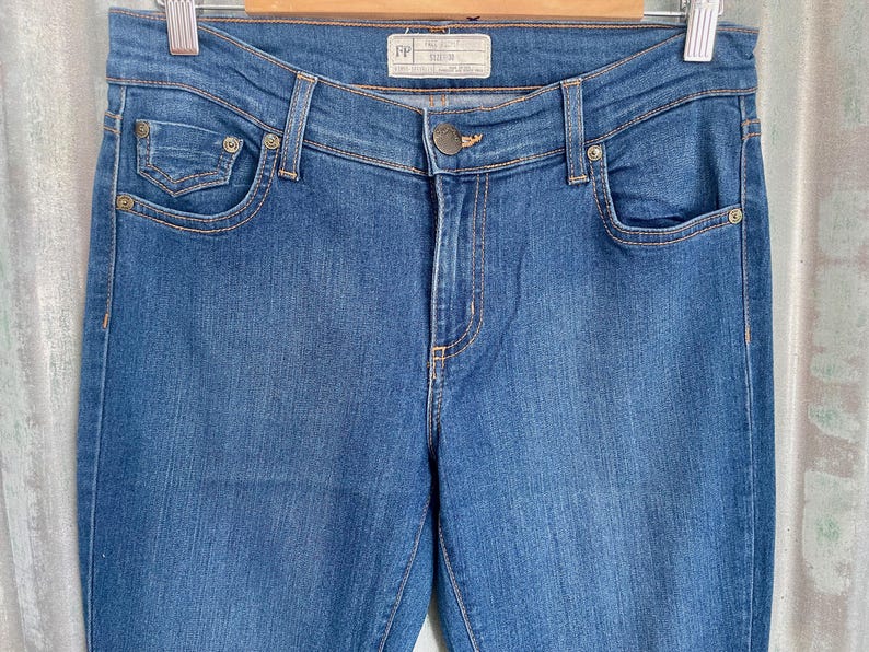 May include: A pair of dark blue denim jeans with a small pocket on the front left leg and a label that reads "FP" on the back waistband.