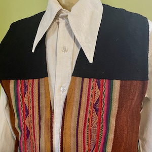 Op de afbeelding: Een zwart en bruin vest met een kleurrijk gestreept patroon. Het vest wordt gedragen over een wit overhemd met knopen en een kraag.