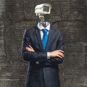 May include: A surreal image of a person in a dark blue suit with a white shirt and blue tie. The person's head is replaced by a white security camera. The background is a textured, dark gray surface.