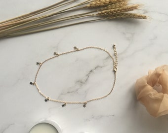 May include: A gold chain necklace with small star charms hanging from it. The necklace is on a white marble surface.