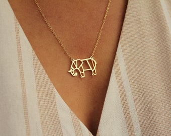 May include: A gold-colored necklace featuring a geometric elephant pendant. The elephant design is made of connected lines, creating a modern, minimalist look. The necklace is worn against a striped beige and white background.