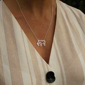 May include: A silver necklace featuring a geometric elephant pendant. The pendant is a stylized outline of an elephant. The necklace is worn over a beige and white striped top.