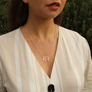 May include: A silver necklace with a pendant shaped like an elephant. The elephant pendant is a geometric design. The necklace is worn over a beige and white striped top.