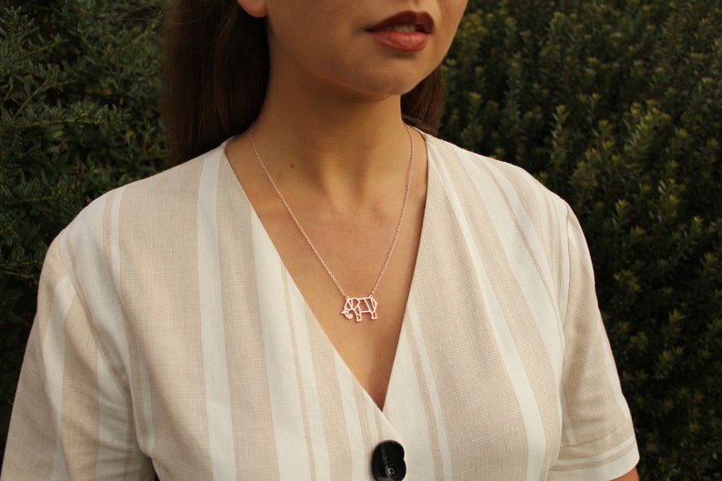 May include: A silver necklace with a pendant shaped like an elephant. The elephant pendant is a geometric design. The necklace is worn over a beige and white striped top.
