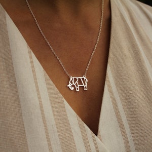 May include: A silver necklace featuring a geometric elephant pendant. The pendant is a stylized, open design with clean lines. The necklace is displayed on a person wearing a beige and white striped top.