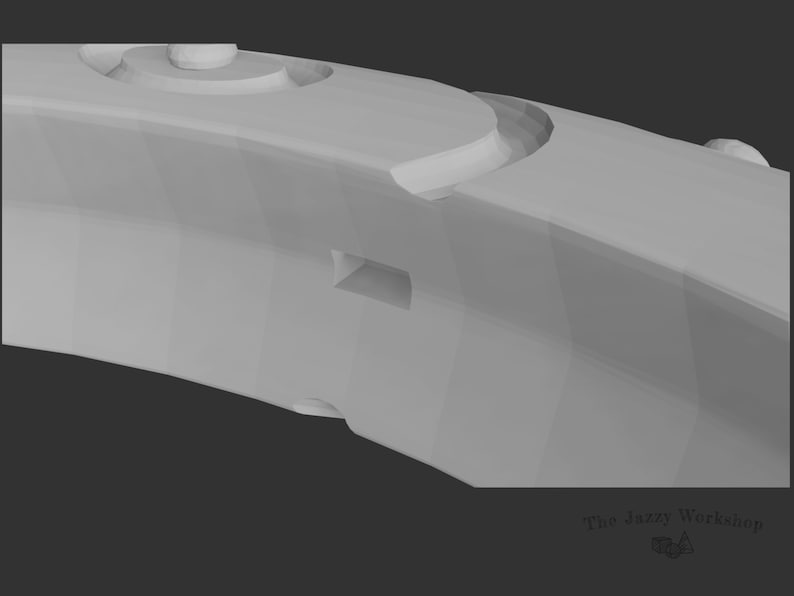 May include: A close-up of a gray, 3D-printed, ring-shaped object with a textured surface and a small, rectangular opening. The object has a series of raised, circular details.