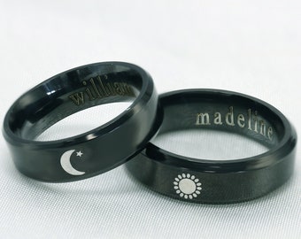 May include: Two black wedding bands with engraved names "william" and "madeline". One band features a crescent moon with a star and the other a sun.