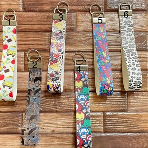 May include: Six key fobs with various designs. The designs include school supplies, a Harry Potter theme, comic book characters, colorful patterns, and a leopard print. Each fob has a metal ring for keys.