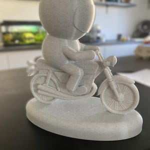 Pode incluir: Uma figura impressa em 3D de cor branca de uma pessoa com capacete a conduzir uma motocicleta. A motocicleta tem a palavra "Suzuki" impressa no lado.