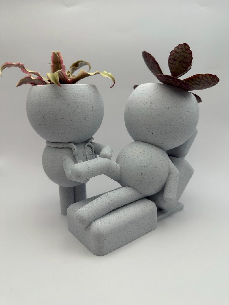Pu&ograve; includere: Un set di vasi grigio chiaro maculato stampato in 3D con due figure stilizzate. Una figura &egrave; in piedi come un medico con uno stetoscopio, mentre l'altra &egrave; sdraiata su un lettino da visita. Ogni testa &egrave; cava e contiene una piccola pianta.