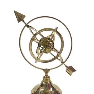 May include: A gold-toned metal armillary sphere with a round base and an arrow pointing upwards. The sphere is made of multiple interlocking rings.