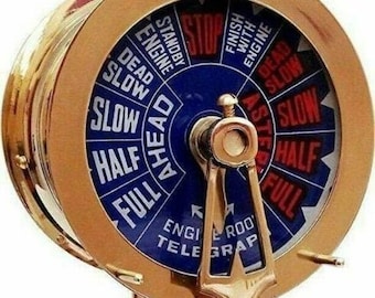 May include: A brass ship's wheel telegraph with a blue and white dial. The dial has markings for "Full Ahead", "Half", "Slow", "Dead Slow", "Stop", "Standby Engine", "Finish With Engine", "Dead Slow", "Slow", "Half", "Full". The telegraph has two wooden handles and a wooden base.