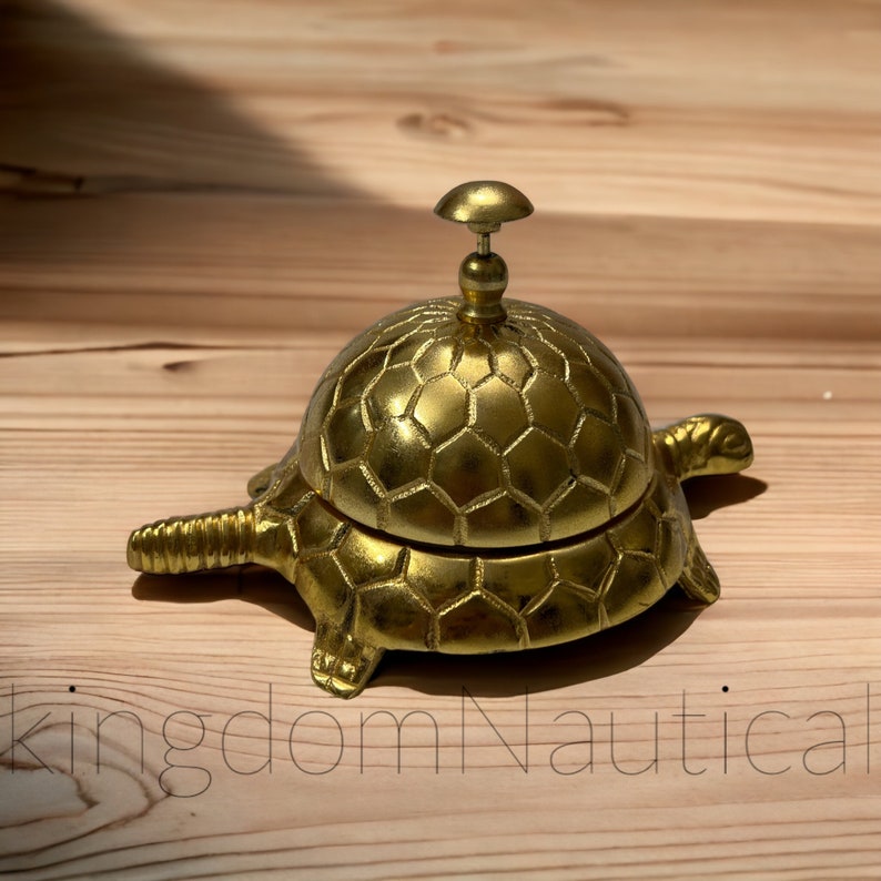May include: A gold-colored turtle-shaped service bell with a hexagonal pattern on the top. The bell is on a wooden surface.