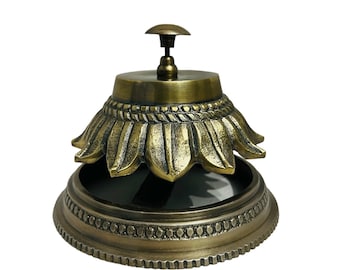 May include: A gold-toned metal bell with a decorative floral design. The bell has a round base and a top with a small knob.