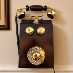 Puede incluir: Un tel&eacute;fono de pared vintage con base de madera oscura y detalles en lat&oacute;n. El tel&eacute;fono tiene un dial giratorio, dos timbres de lat&oacute;n y un cable negro. El auricular tiene un mango de madera oscura y auriculares de lat&oacute;n.