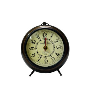 May include: A black and gold tabletop clock with Roman numeral markings and a red hour hand. The clock face reads "Huntley Station, Cambridge England 1924".