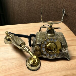 May include: A vintage-style rotary phone with an ornate gold finish and a black cord. The phone has a circular dial with numbers 1 through 0.