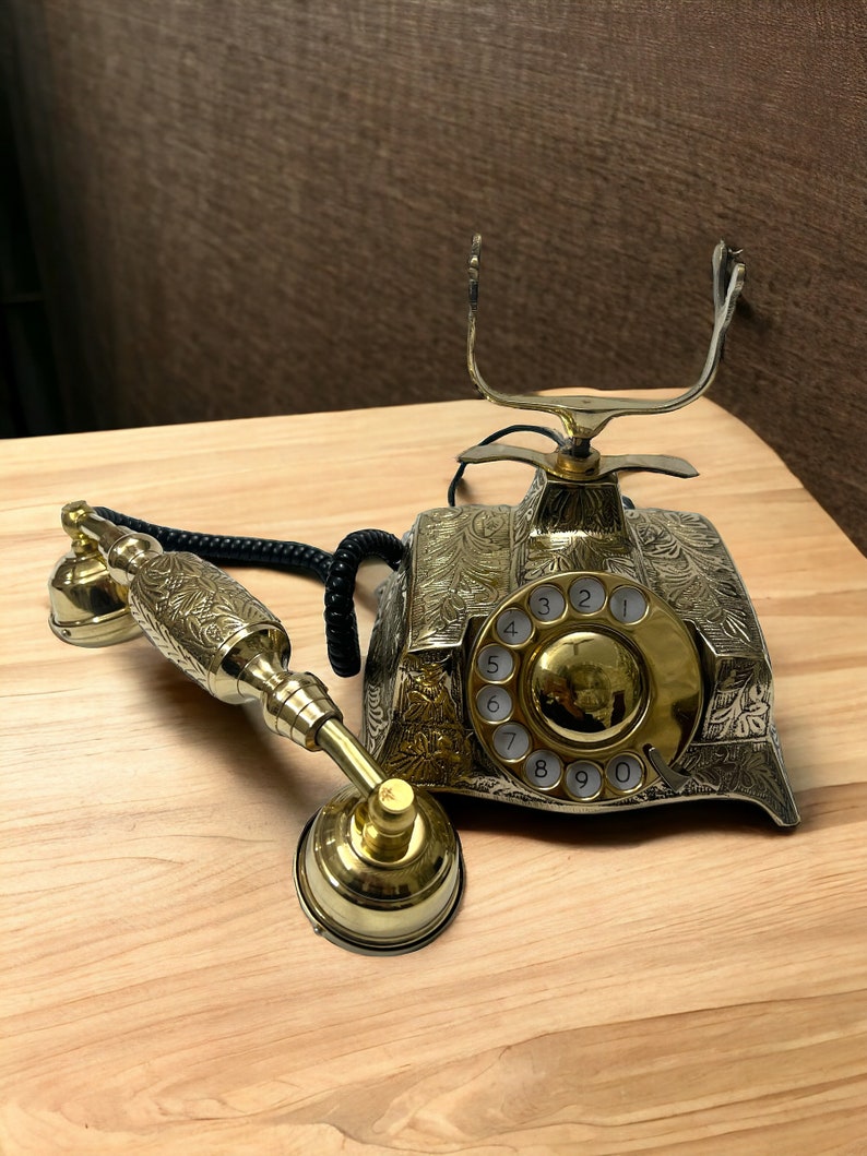 May include: A vintage-style rotary phone with an ornate gold finish and a black cord. The phone has a circular dial with numbers 1 through 0.