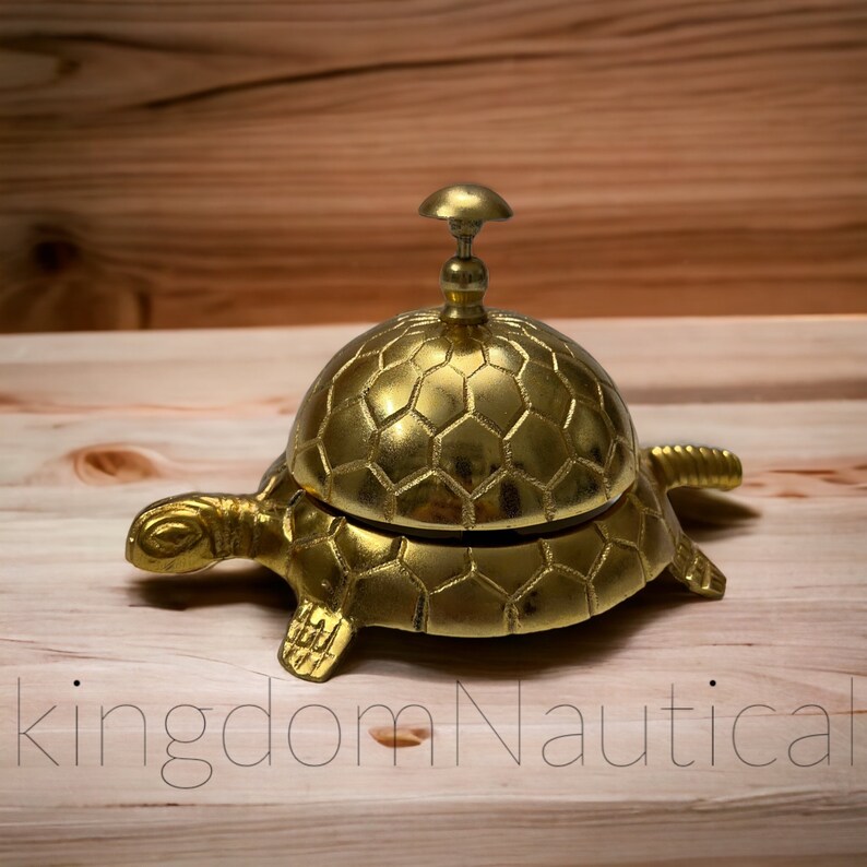 May include: A gold-colored turtle-shaped service bell with a hexagonal pattern on the top. The bell is made of metal and has a small knob on top.