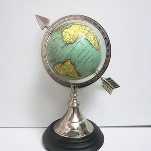 May include: A silver globe with a black base and a silver arrow pointing to the South Atlantic Ocean. The globe is on a white background.