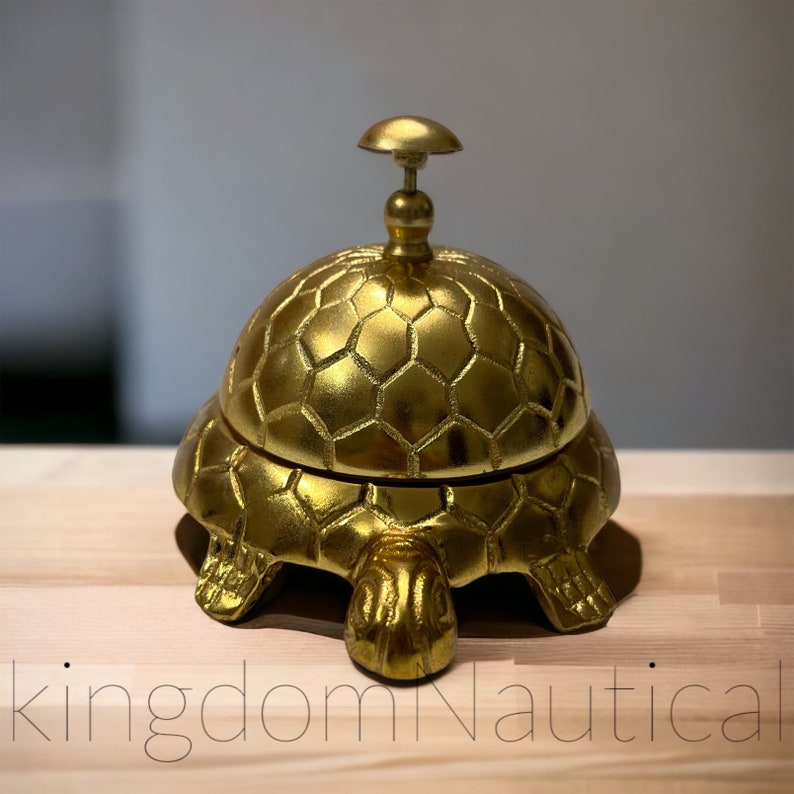 May include: A gold-colored turtle-shaped service bell with a hexagonal pattern on the top. The bell is made of metal and has a shiny finish.