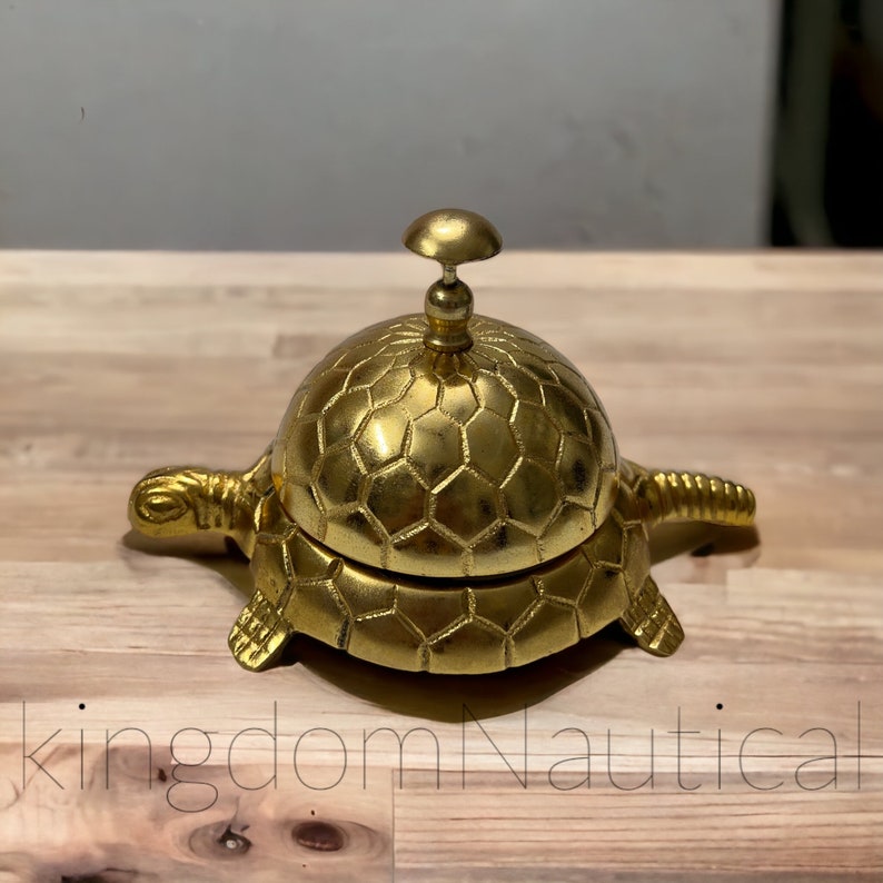 May include: A gold-colored turtle-shaped service bell with a hexagonal pattern on the shell. The bell is on a wooden surface.