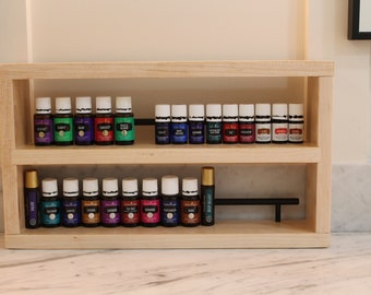 May include: A wooden shelf unit with two shelves, holding rows of small glass bottles with white caps. The bottles are filled with colourful liquids. The shelf unit is on a white countertop.