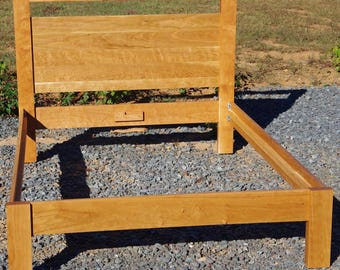 May include: A wooden bed frame with a simple design. The frame is made of solid wood and has a natural finish. The headboard is tall and rectangular, with a slightly curved top. The footboard is low and has a straight top.