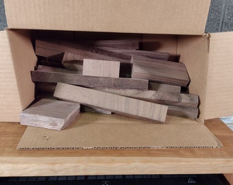 Op de afbeelding: Een kartonnen doos gevuld met verschillende stukken hout. Het hout is lichtbruin van kleur met donkerbruine strepen. De doos is open en het hout valt eruit.