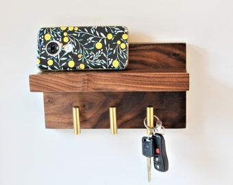 May include: A wooden key holder with three brass hooks and a shelf on top. A phone with a floral case is on the shelf.