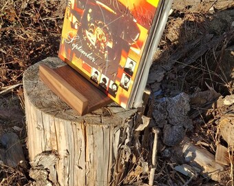 May include: A wooden record holder displaying a vinyl record album. The album cover features a vibrant orange and yellow design with the word "September" visible. The holder is placed on a tree stump.