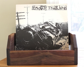 May include: A dark wood record stand with a black and white vinyl record inside. The record cover features a black and white image of a train wreck with the text "End of the Line".