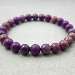 Puede incluir: Un brazalete de piedras preciosas de color púrpura con cuentas redondas. Las cuentas tienen un patrón de mármol y un acabado brillante.