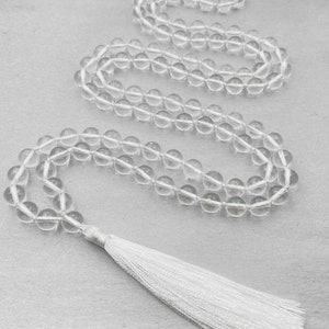 Puede incluir: Un collar mala de cuentas de cristal transparente con un borla blanca. El collar est&aacute; hecho de cuentas redondas y tiene aproximadamente 108 cuentas.
