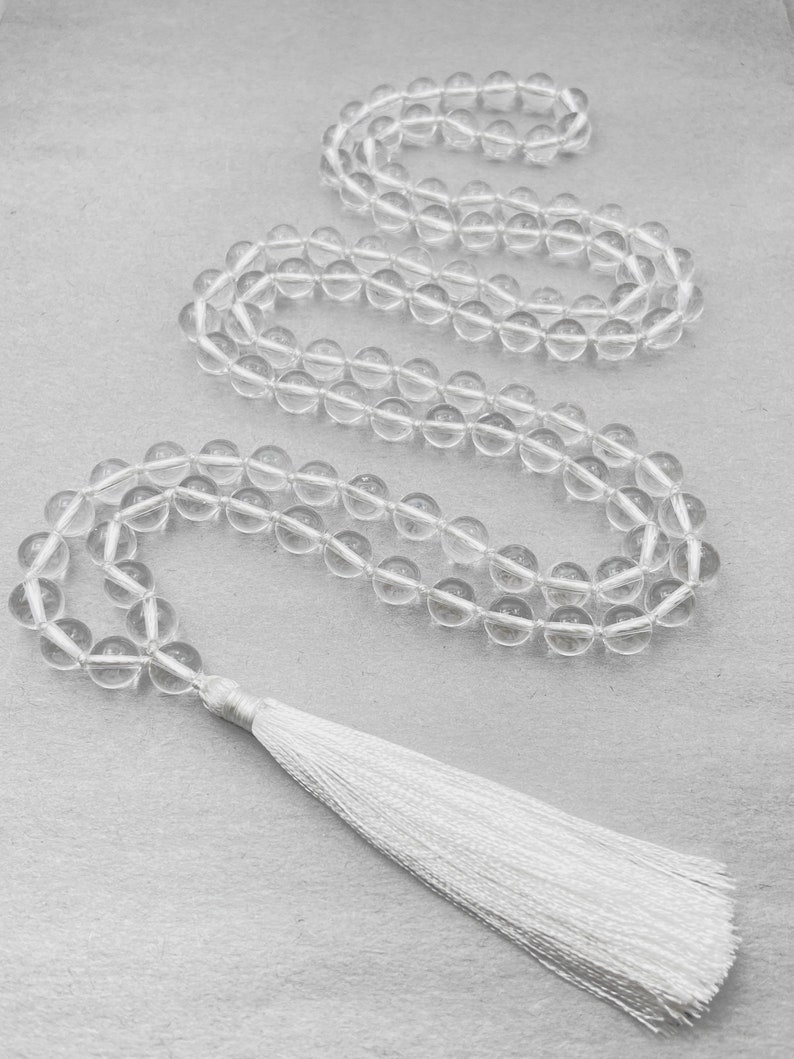Puede incluir: Un collar mala de cuentas de cristal transparente con un borla blanca. El collar est&aacute; hecho de cuentas redondas y tiene aproximadamente 108 cuentas.