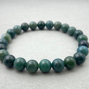 Puede incluir: Un brazalete de cuentas de ágata verde con cuentas redondas. El brazalete está hecho de piedra natural y tiene un color verde oscuro con acentos verde claro.
