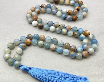 May include: A long beaded necklace with a blue tassel. The necklace features round, light blue, brown, and white beads strung on a blue cord. The tassel is a vibrant blue color.