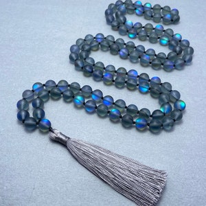 Puede incluir: Un collar de cuentas grises iridiscentes con un borla de plata. Las cuentas son redondas y tienen un brillo sutil.