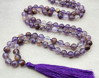 May include: A purple amethyst mala with a purple tassel. The beads are round and have a clear, translucent appearance with hints of brown and white.