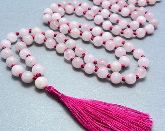 May include: A pink rose quartz mala necklace with a pink tassel. The necklace is made of 108 beads and is strung on a pink cord.