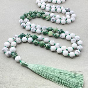 May include: A long green and white beaded necklace with a green tassel. The beads are made of green and white stone.
