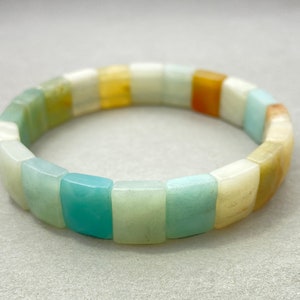 Puede incluir: Un brazalete hecho de cuentas cuadradas en tonos de verde, blanco y amarillo.