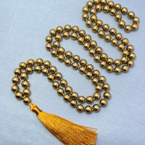 May include: A gold beaded necklace with a gold tassel. The necklace is made of round beads and is approximately 30 inches long.