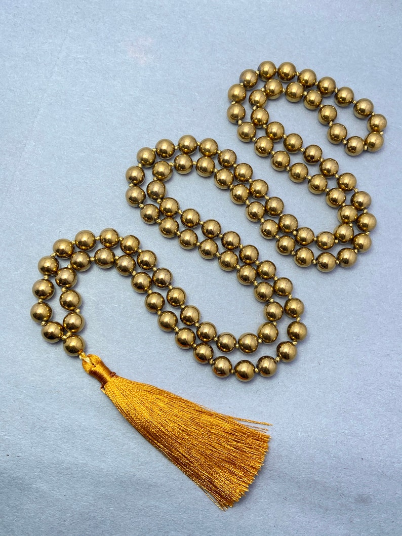 May include: A gold beaded necklace with a gold tassel. The necklace is made of round beads and is approximately 30 inches long.