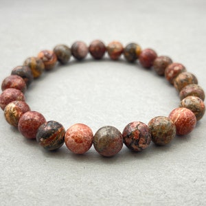Pode incluir: Um bracelete feito de contas salpicadas de marrom, vermelho e branco.