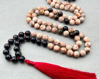 May include: A mala or prayer bead necklace with a red tassel. The beads are made of black obsidian, tiger's eye, and a white and brown marbled stone.